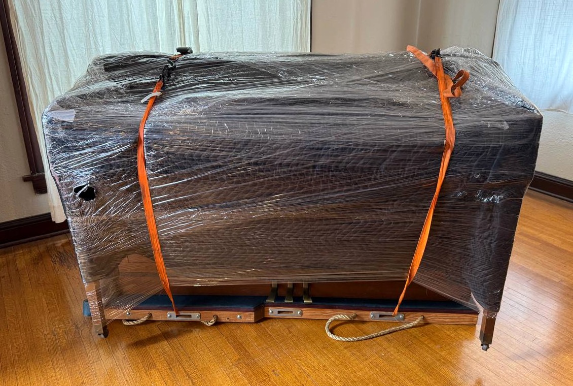 Wrapped piano secured on a skid inside a home before transport