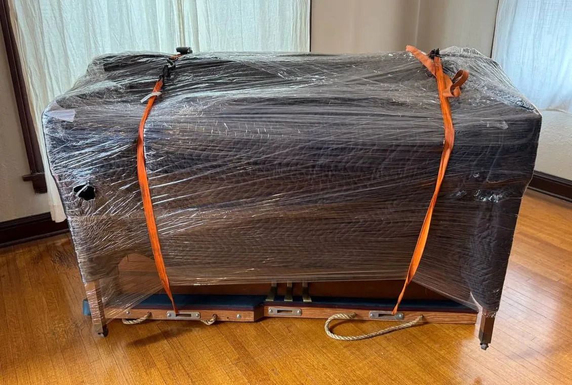 Wrapped piano secured on a skid inside a home before transport